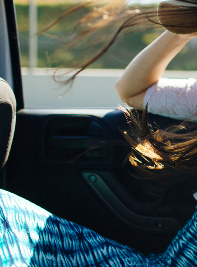 Girl in the backseat of a car, caught in a joyous moment as the mind blows through her long brown hair.